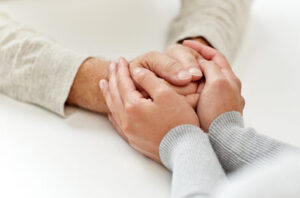 Die Hände einer älteren Person werden helfend von den Händen einer jüngeren Person umschlossen.