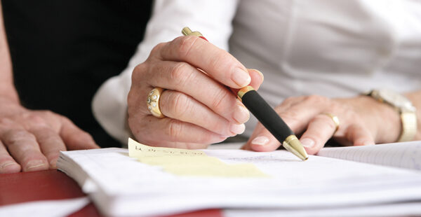 Nahaufnahme einer Hand, die mit einem Kugelschreiber etwas unterzeichnet.